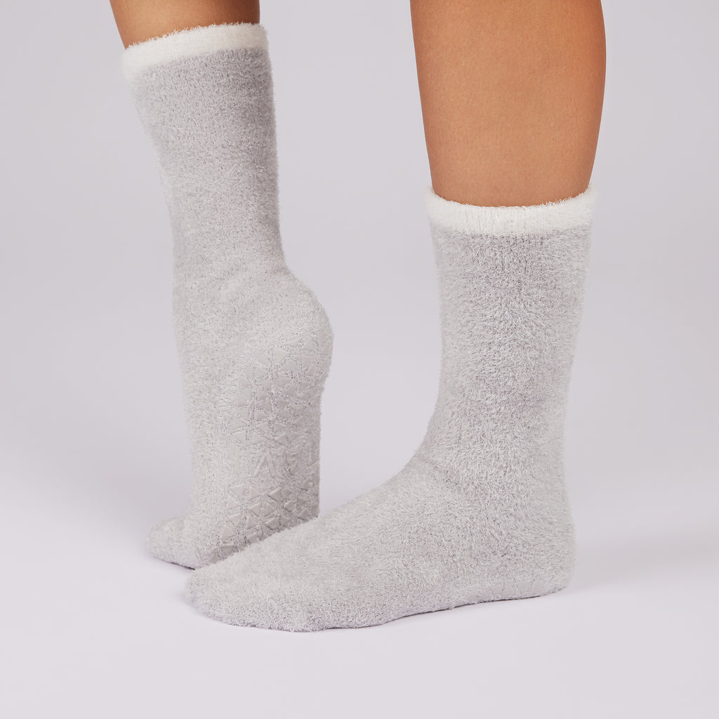 Gray fuzzy non slip sole socks with white cuffs on a light gray background