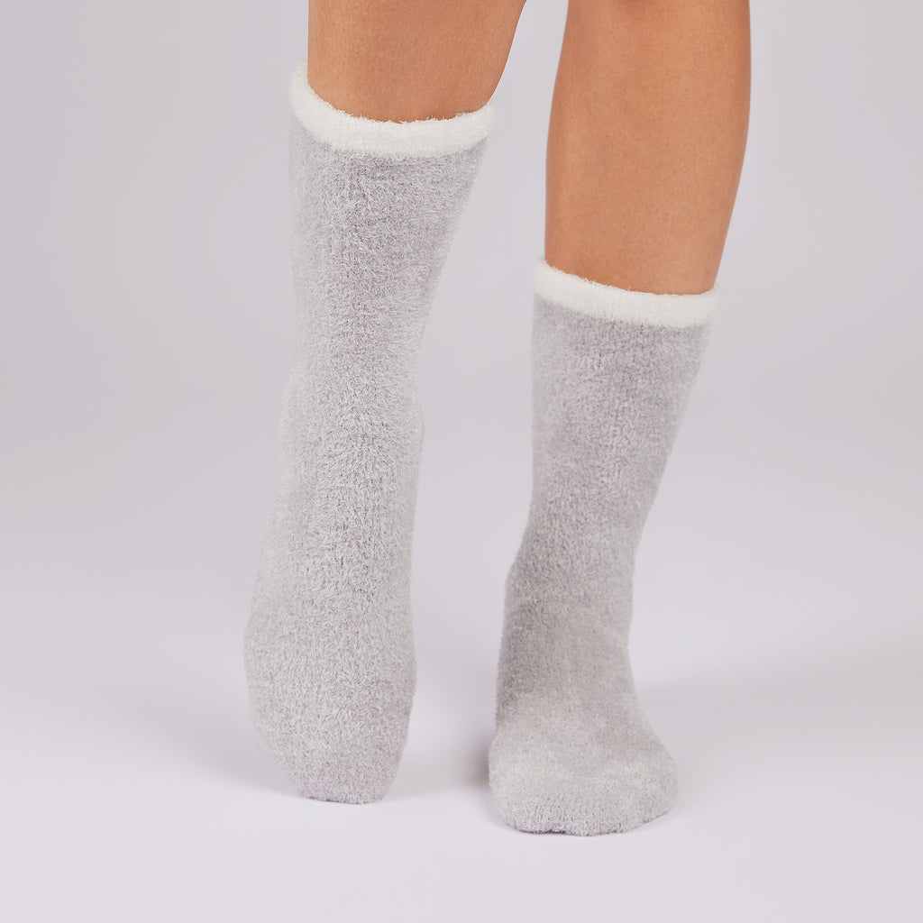 Gray fuzzy socks with white cuffs worn by a person on a light gray background