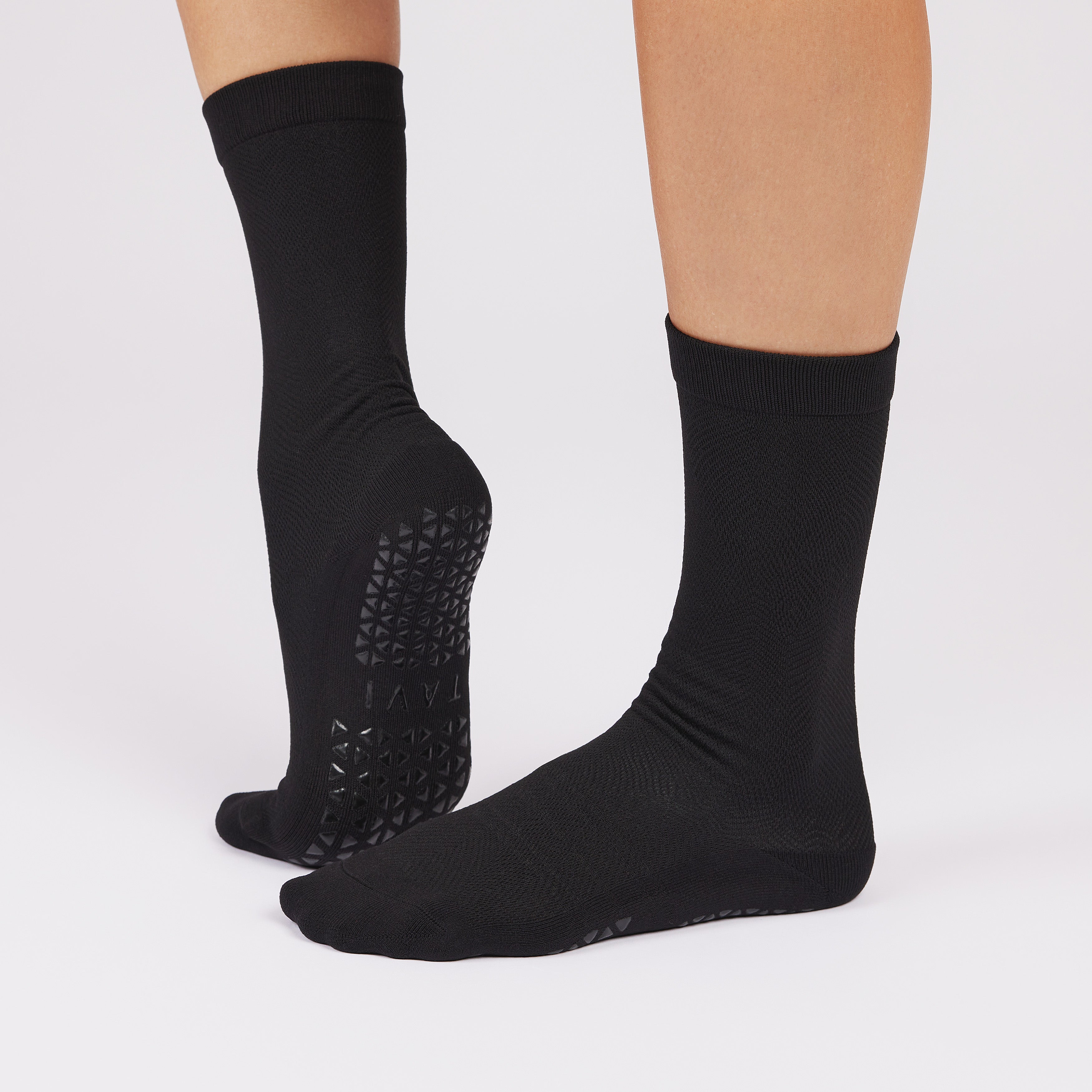 Black socks with non slip sole worn by a person on a light gray background